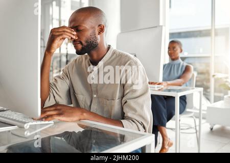 Junger gestresster afroamerikanischer Geschäftsmann, der bei der Arbeit an einem Desktop-Computer Kopfschmerzen hatte. Ein unglücklicher männlicher Geschäftsmann Stockfoto
