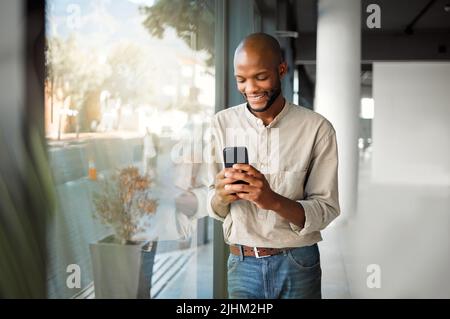 Fröhlicher afroamerikanischer Geschäftsmann, der bei der Arbeit eine Nachricht auf ein Telefon schreibt. Glücklicher männlicher Business-Profi mit Social Media auf einem Handy, während Stockfoto