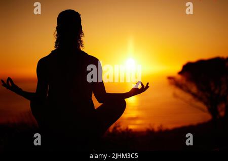 Rückansicht Silhouette Yoga Frau meditiert mit Beinen gekreuzt für Outdoor-Praxis in abgelegener Natur. Achtsame Person, die allein sitzt und ausbalanciert Stockfoto