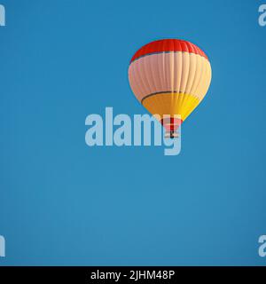 Einsamer Heißluftballon fliegt in blauem Himmel. Stockfoto