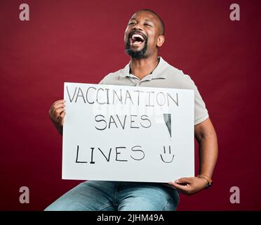 afroamerikanischer covidgeimpfter Mann, der Poster zeigt und hält. Schreiender schwarzer Mann isoliert auf rotem Studiohintergrund mit Copyspace. Aufgeregtes Modell Stockfoto