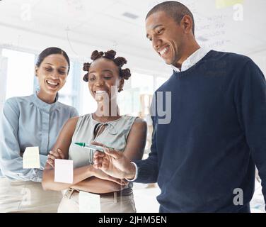Drei glückliche, vielfältige Geschäftsleute, die bei der Arbeit in einem Büro Ideen schreiben und Brainstorming durchführen. Fröhlicher hispanischer Geschäftsmann, der eine Notiz auf einem macht Stockfoto