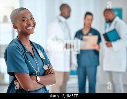 Reife afroamerikanische Ärztin, die während der Arbeit in einem Krankenhaus mit gekreuzten Armen steht. Ein Experte Arzt lächelt während Stockfoto