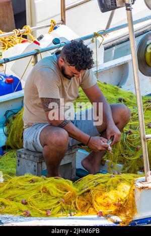 griechischer Fischer auf der Insel kreta flicken Netze auf seinem Boot in einem Hafen im Abendlicht, griechischer Fischer im Boot reparieren Ausrüstung für morgen Stockfoto