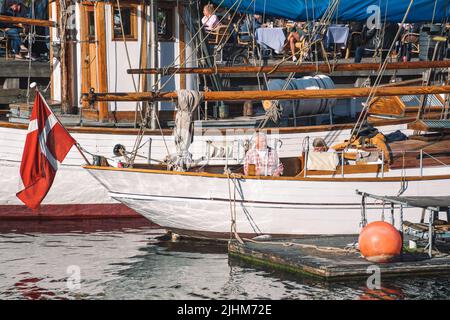 Altes Holzboot mit dänischer Flagge und Einheimischen entlang des Nyhavn-Kanals oder des Neuen Hafens, Hafenviertel aus dem 17.. Jahrhundert, Kopenhagen, Dänemark Stockfoto