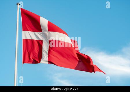 Schöne Flagge Dänemarks oder dänische Flagge unter der Sonne auf einem Fahnenmast mit blauem Himmel auf dem Hintergrund, Nahaufnahme Stockfoto