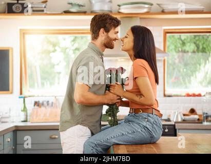 Junge Content kaukasischen Freund gibt seiner fröhlichen gemischten Rasse Freundin einen Blumenstrauß zu Hause. Glückliche hispanische Frau erhält Rosen von ihr Stockfoto