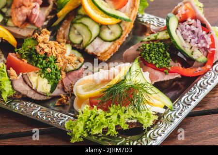 Traditionelle dänische Smørrebrød oder offene Sandwiches auf einem Teller, Roastbeef mit Remoulade, Tomaten und geriebenem Meerrettich auf dänischem Roggenbrot Stockfoto