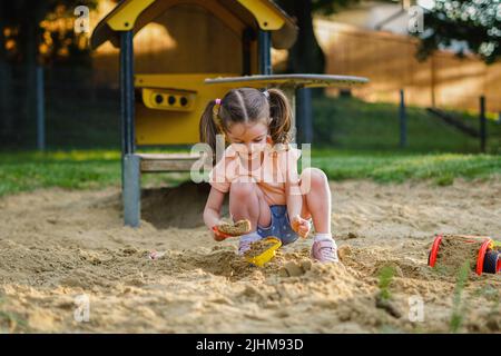 Schönes Baby mit Spaß an sonnigen warmen Sommertag - nettes Kleinkind Mädchen spielen im Sand auf Spielplatz im Freien Stockfoto