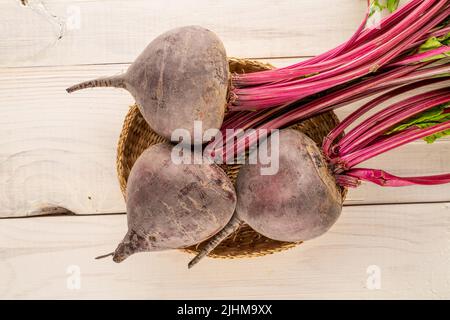 Drei süße rote Rüben in einer Strohplatte auf einem Holztisch, Nahaufnahme, Draufsicht. Stockfoto