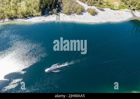 Luftaufnahme des Lovatn-Sees, lokales Schiff auf dem Weg nach Kjenndalstova, Schotterbergstraße über dem See, Norwegen. Stockfoto