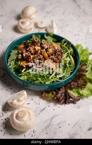 Warmer Salat mit Pilzen und Rucola auf grauem Hintergrund. Stockfoto