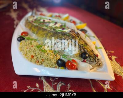 Im Restaurant wird ganzer Fisch gebackener Hechtbarsch auf einer weißen Platte serviert. Stockfoto