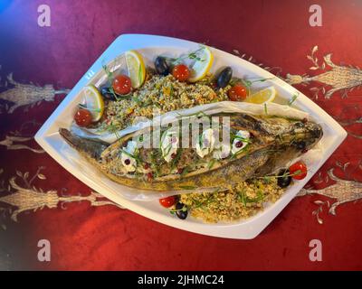 Im Restaurant wird ganzer Fisch gebackener Hechtbarsch auf einer weißen Platte serviert. Stockfoto