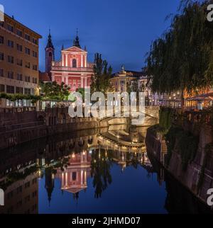 Ljubljana, Slowenien - beleuchtete Tromostovje-Brücke und Franziskanerkirche der Verkündigung mit dem Fluss Ljubljanica im Stadtzentrum von Ljubljana, Stockfoto