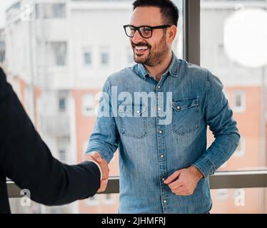 Glückliche Profis, die nach einem erfolgreichen Deal die Hände schütteln. Geschäftspartner gratulieren zu dem Treffen. Sie stehen vor dem Fenster des Korporat Stockfoto