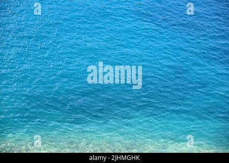 Die blaue Meerwasseroberfläche mit den Steinen auf dem Grund. Klares türkisfarbenes Wasser als Hintergrund Stockfoto