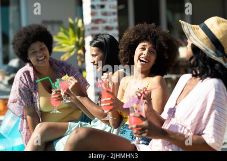 Fröhliche Biracial Freundinnen mit Cocktails reden und Spaß haben, während das Wochenende genießen Stockfoto