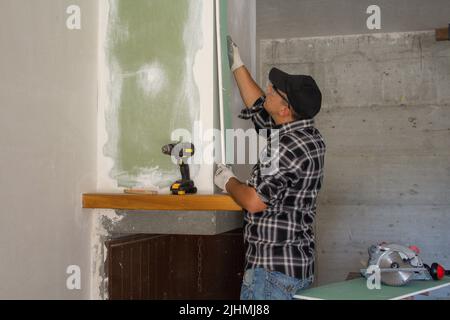 Abbildung eines Handwerkers, der Trockenbauplatten installiert. Do-it-yourself manuelle Arbeit der Renovierung eines Kamins und Hauswände Stockfoto