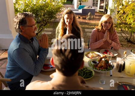 Bild einer mehrgenerationsigen kaukasischen Familie, die vor dem Abendessen im Freien betet Stockfoto
