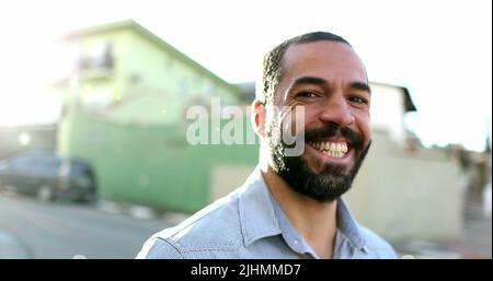 Hispanischer Mann lächelt vor der Kamera, die draußen auf der Straße steht. Südamerikanische Person Portrait Lächeln Stockfoto