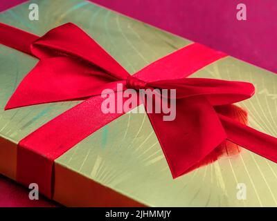 Nahaufnahme der goldenen Schokoladenbox mit rotem Band Stockfoto