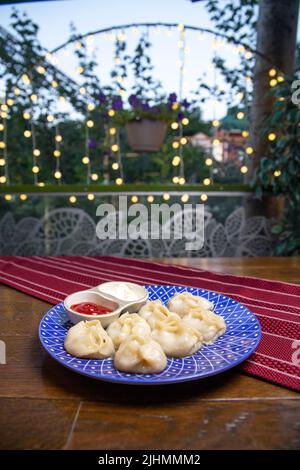 manti und Sauce auf einem blauen Teller auf einem Burgund Hintergrund Stockfoto