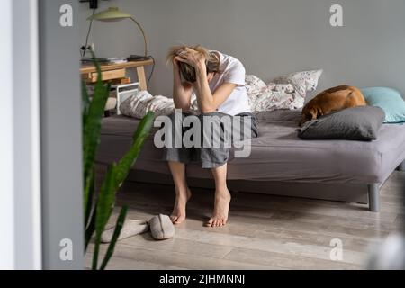 Unglückliche Frau, die morgens auf dem Sofa sitzt und den Kopf in den Händen hält und an Kater-Kopfschmerzen leidet Stockfoto