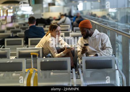 Internationales junges Paar sucht in Handy Online Check-in in der App, tauschen Kontakte untereinander Stockfoto