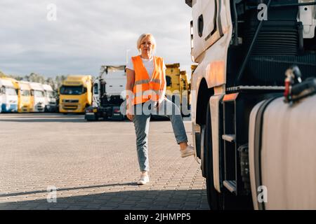 Kaukasische Frau mittleren Alters vor einem gelben Sattelschlepper auf einem Parkplatz Stockfoto