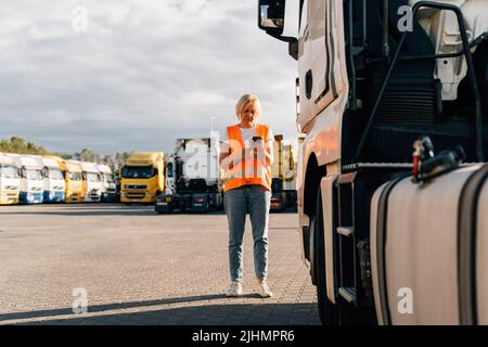 Kaukasische Frau mittleren Alters, die vor einem gelben Sattelschlepper telefoniert Stockfoto