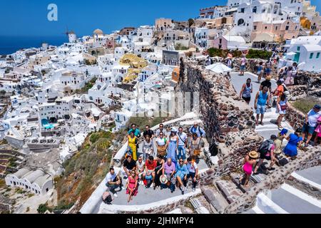 Gruppe von Touristen, die sich mit einem Teil des Dorfes Oia im Hintergrund ausruhen. Santorini, Kykladen, Ägäis, Griechenland. Stockfoto