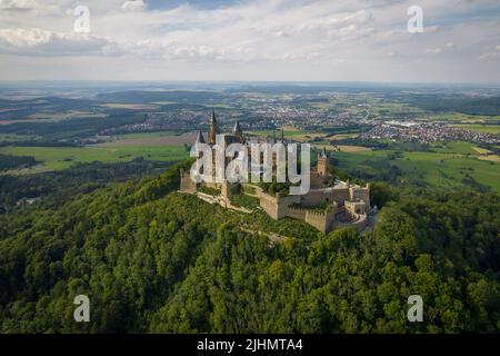 Drohnenaufnahme der Burg Hohenzollern auf dem bewaldeten Gipfel der Schwäbischen Alpen im Sommer. Landschaftlich schöne Luftaufnahme der alten deutschen Burg. Berühmtes märchenhaftes gotisches Wahrzeichen in Stuttgarts Umgebung Stockfoto