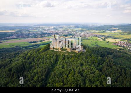 Drohnenaufnahme der Burg Hohenzollern auf dem bewaldeten Gipfel der Schwäbischen Alpen im Sommer. Landschaftlich schöne Luftaufnahme der alten deutschen Burg. Berühmtes märchenhaftes gotisches Wahrzeichen in Stuttgarts Umgebung Stockfoto