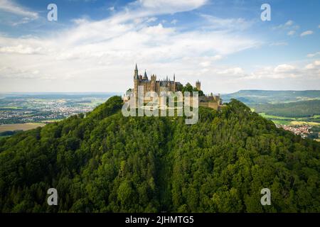 Drohnenaufnahme der Burg Hohenzollern auf dem bewaldeten Gipfel der Schwäbischen Alpen im Sommer. Landschaftlich schöne Luftaufnahme der alten deutschen Burg. Berühmtes märchenhaftes gotisches Wahrzeichen in Stuttgarts Umgebung Stockfoto