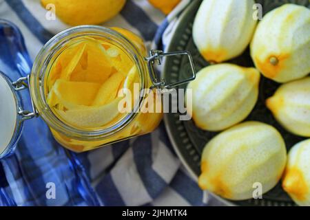 Glas mit Zitronenschale im Inneren, neben frisch geschälten Zitronen. Selektiver Fokus. Zubereitung von hausgemachtem Limoncello-Likör, traditioneller italienischer Zitrone Stockfoto