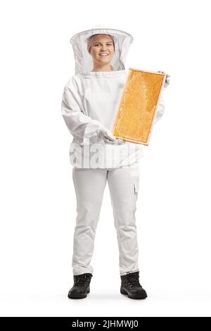 In voller Länge Porträt einer jungen Bienenhalterin in einer Uniform, die einen auf weißem Hintergrund isolierten Wabenrahmen hält Stockfoto