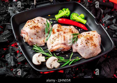 Rohe Hähnchenschenkel in einer Pfanne mit Gemüse und Gewürzen stehen auf einem heißen Barbecue-Grill. Bio-Fleisch Stockfoto