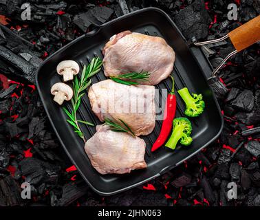 Rohe Hähnchenschenkel in einer Pfanne mit Gemüse und Gewürzen stehen auf einem heißen Barbecue-Grill. Bio-Fleisch Stockfoto