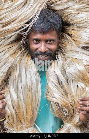 20. Juli 2022, Manikganj, Dhaka, Bangladesch: Arbeiter tragen 50kg Pakete frisch geernteter Jute über ihren Köpfen, um sie auf einem Markt in Manikganj, Bangladesch, zu verkaufen. Die Golden Fiber of Bangladesh, Jute bietet eine Alternative zu Plastiktüten wegen seiner biologisch abbaubaren Eigenschaften. Die fleißigen Arbeiter scheinen große goldene Perücken zu tragen, und ihre Körper sind von den schweren Naturfasern umhüllt, wobei nur ihre Gesichter sichtbar sind, da sie jeweils etwa 50kg Jute auf ihren Schultern tragen. Bangladesch ist nach Indien der zweitgrößte Produzent von Jute und der größte Exporteur von Jute- und Juteprodukten Stockfoto