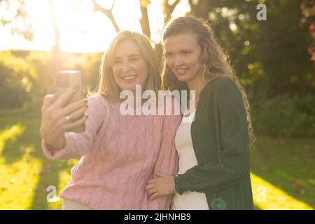 Bild einer glücklichen kaukasischen Mutter und einer erwachsenen Tochter, die im Herbstgarten Selfie macht Stockfoto