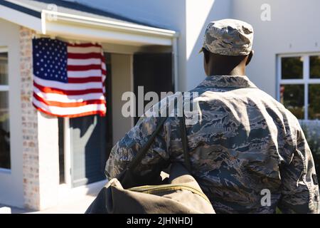 Rückansicht eines Soldaten in Tarnkleidung mit Rucksack, der vor dem Haus im Hof steht Stockfoto