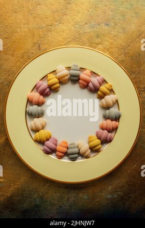 Bunte Muschelschalen 'Conchiglioni' Pasta-Arrangement im Kreis auf goldgelber Platte mit Kopierfläche in der Mitte Stockfoto