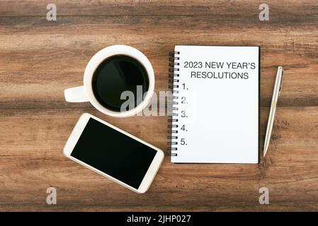 2023 Neujahrsauflösung Text auf Notizblock mit Smartphone, Stift und Tasse Kaffee Stockfoto