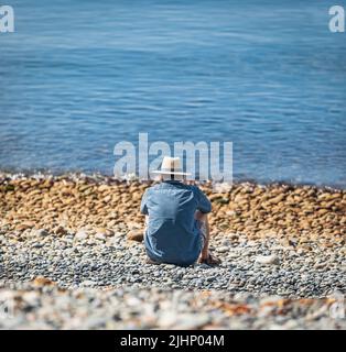 Mann genießt am Strand an einem Sommertag im Urlaub. Mann im Hut, der sich an einem sonnigen Tag am Strand entspannt. Reisefoto, selektiver Fokus Stockfoto