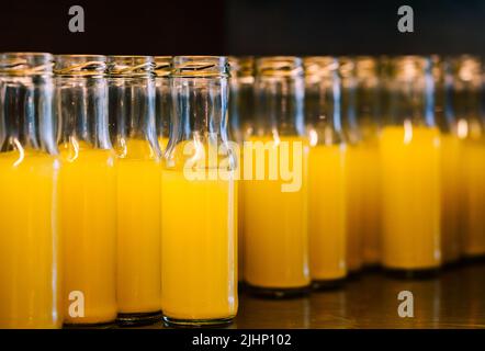 Nahaufnahme einer Gruppe von frischem Ananassaft in kleinen Glasflaschen, kaltem frischem Ananassaft in einem Glasbehälter auf einem Regal aus Edelstahl. Stockfoto
