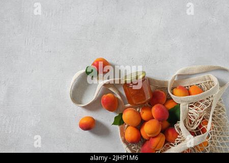 Aprikosen im Saitenbeutel und Glas mit Aprikosenmarmelade auf weißem Tisch. Kopierraum. Draufsicht Stockfoto