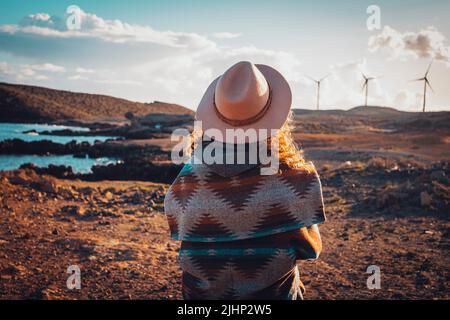 Rückansicht einer Frau, die die Landschaft mit Windmühlen-Turbinen im Hintergrund bewundert. Konzept der Reise und Fernweh Menschen in malerischen Ort während Sonnenuntergang tim Stockfoto