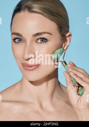 Face Jade Roller. Gesicht der schönen Frau mit grünem Jaderolle für Anti-Aging-Verfahren Stockfoto