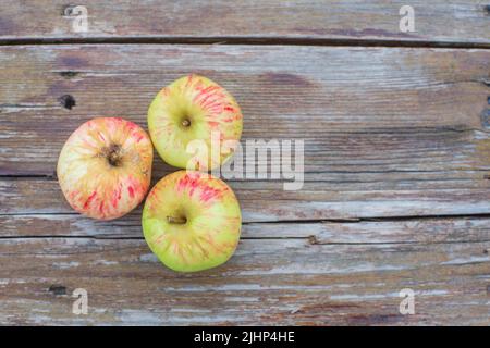 Drei frische Äpfel liegen auf einer hölzernen Oberfläche. Gesundes Lebensmittelkonzept Stockfoto
